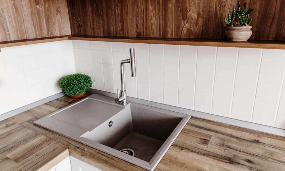 Stylish gray sink with metal faucet on modern kitchen with wooden tabletop and plants. Good if buying a kitchen sink in Scandanavian style